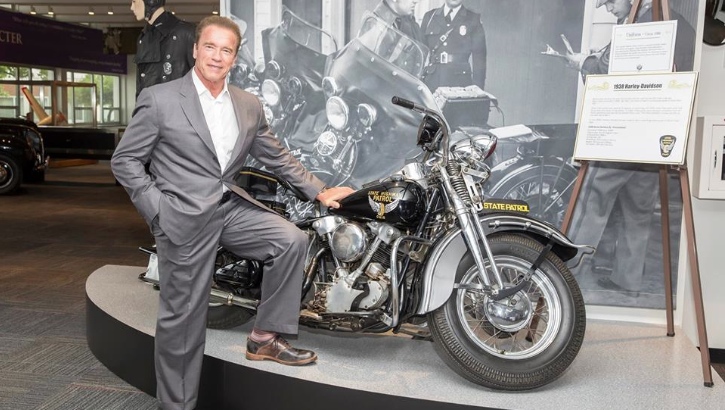 Arnold Schwarzenegger next to a classic motorcycle at Ohio Highway Patrol Musem