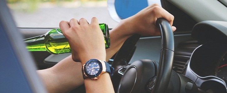 Person drinking alcohol while sitting on the driver's seat in a vehicle and holding the steering wheel (this is against the law in many countries, btw)