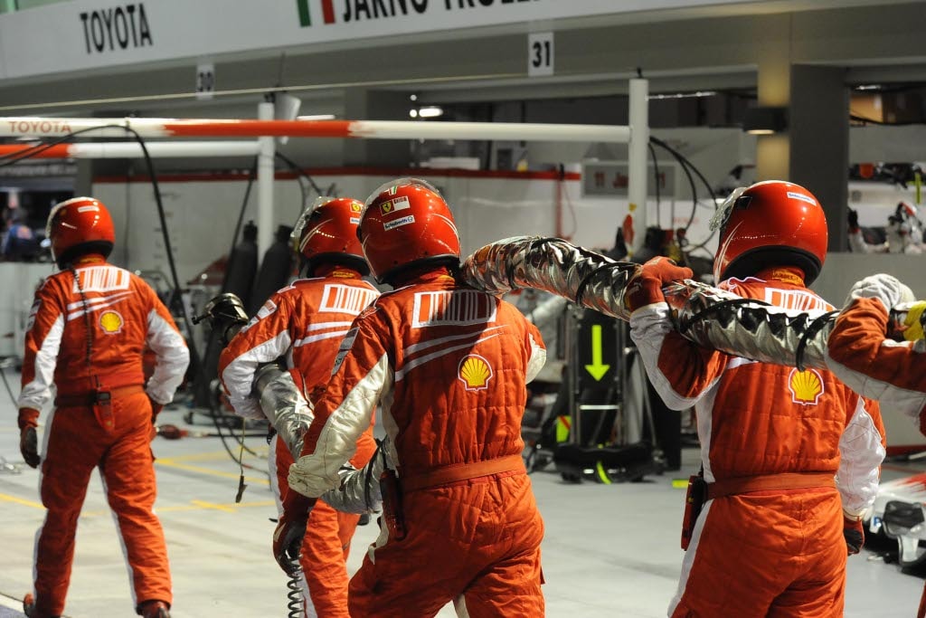 Ferrari mechanics on their way back to the pit box, fuel hose included