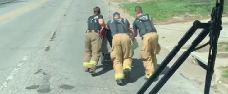 Firefighters push man in wheelchair home, with fire truck driving behind them for safety