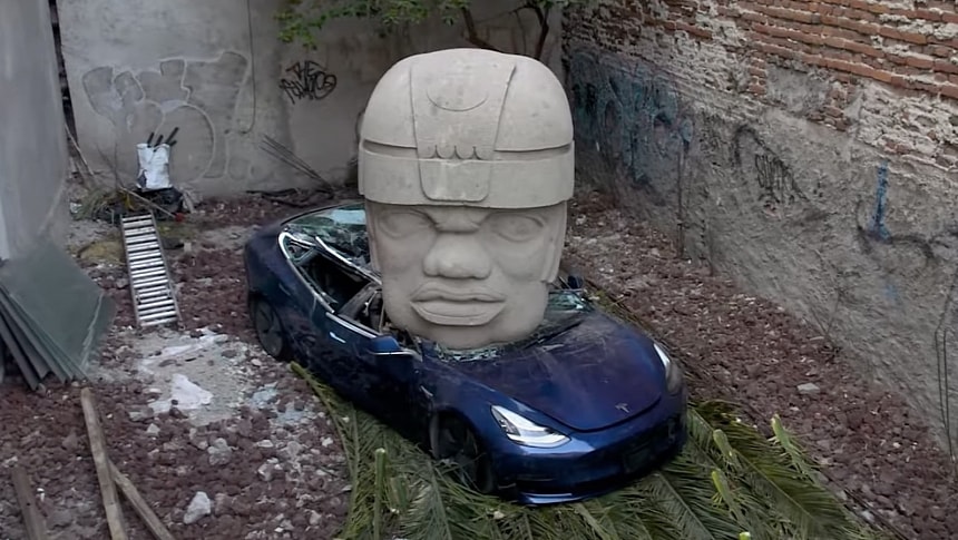 Giant stone head sculpture crushes Tesla Model 3