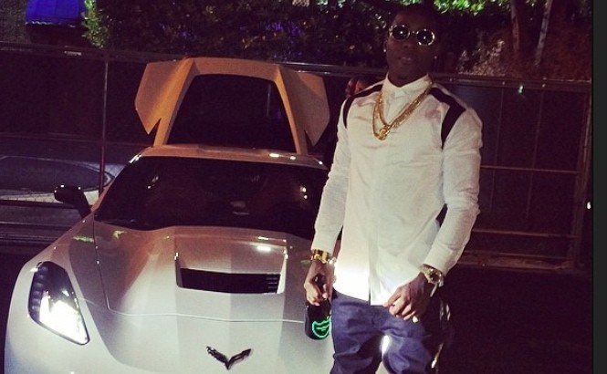 Ace Hood holding a bottle of champagne next to his ride